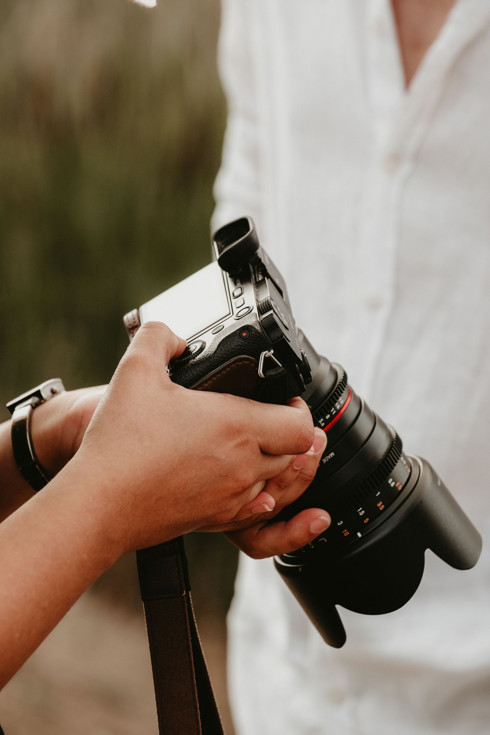 Close-up shot of hands holding a DSLR camera outdoors, focusing on the lens and equipment.